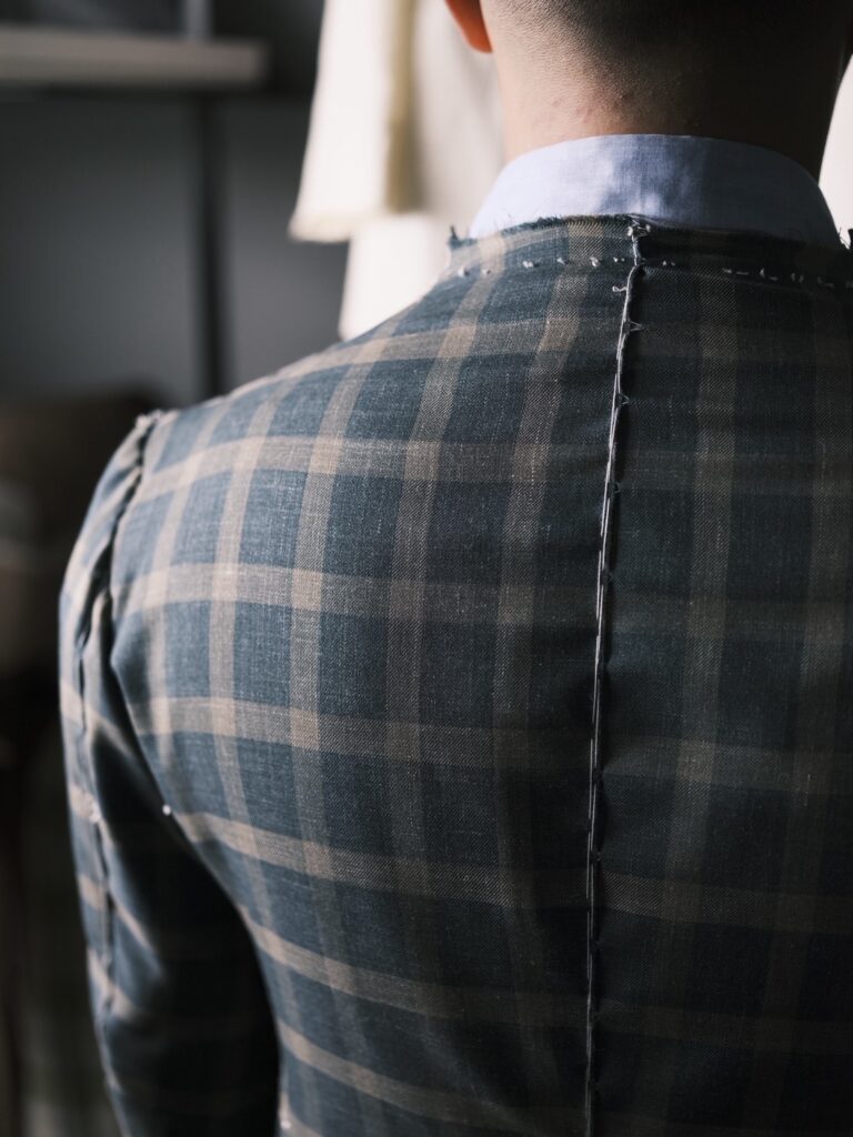 正裝定義的裁縫細節：裁縫師在格紋布料西裝背部使用疏縫線，展示量身訂製的肩線與結構調整。